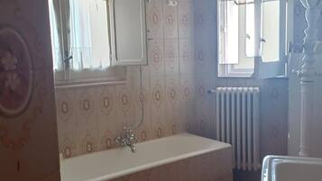 Ein Badezimmer mit Badewanne, Spiegel, Heizkörper und Fenster.