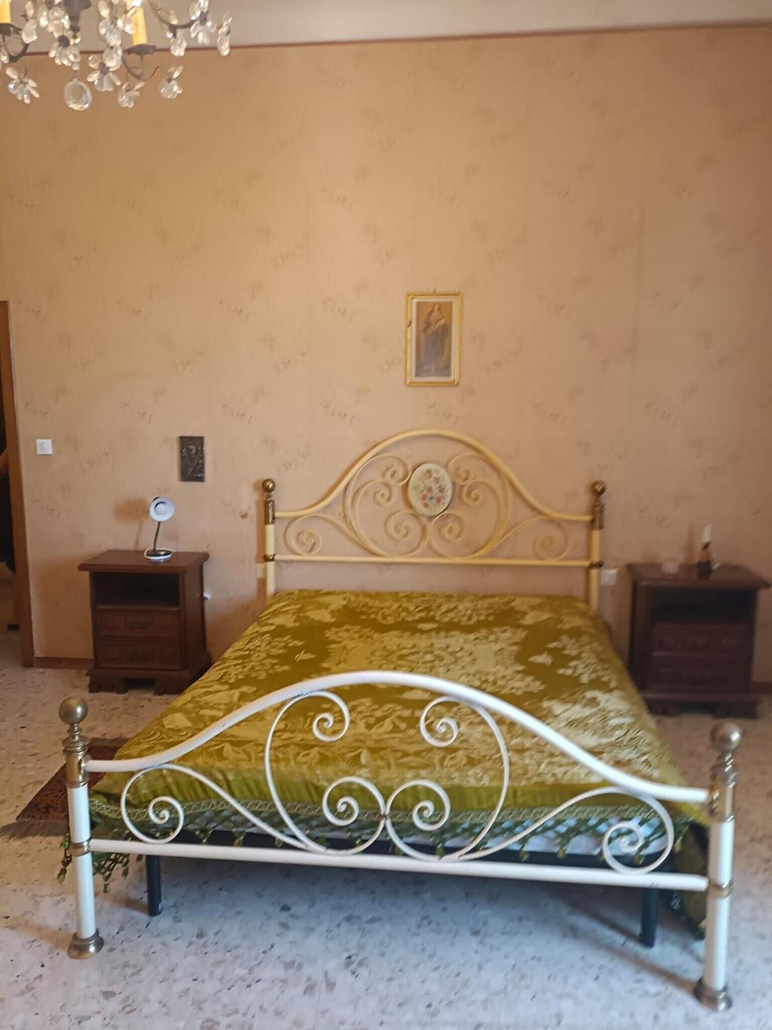 A bed with a metal frame and a patterned bedspread, two nightstands, a wall clock, and a framed picture.