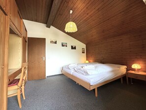 A bedroom with a wooden ceiling, a bed, a nightstand with a lamp, and a wardrobe. - Clabina 32 # 6-bed apartment, Bad, WC 6-Bettwohnung, Bad, WC by Interhome (Leukerbad)