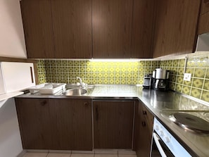 Een kleine keuken met houten kastjes, een roestvrijstalen spoelbak en een koffiezetapparaat.
