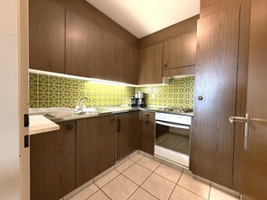 A compact kitchen with wooden cabinets, a stainless steel sink, a coffee maker, and a built-in oven. - Clabina 32 # 6-bed apartment, Bad, WC 6-Bettwohnung, Bad, WC by Interhome (Leukerbad)