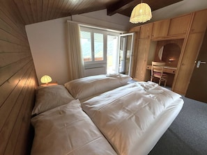 Une chambre avec un grand lit, des murs en bois, une fenêtre avec des rideaux et une armoire en bois.