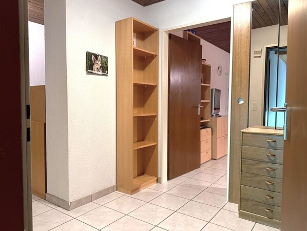 Een gang met houten schapenkasten, een betegelde vloer en een deur naar een andere kamer.