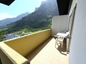 A balcony with a view of a mountainous landscape, a table, and two chairs. - Clabina 32 # 6-bed apartment, Bad, WC 6-Bettwohnung, Bad, WC by Interhome (Leukerbad)