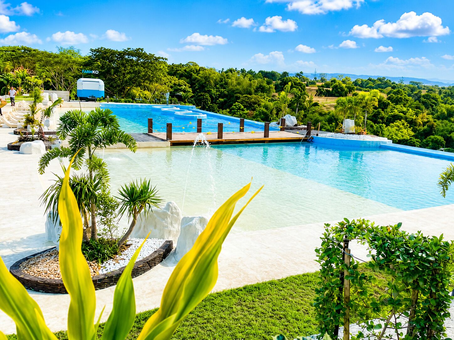 Una grande piscina all'aperto con un molo, circondata da vegetazione lussureggiante e un cielo azzurro terso.