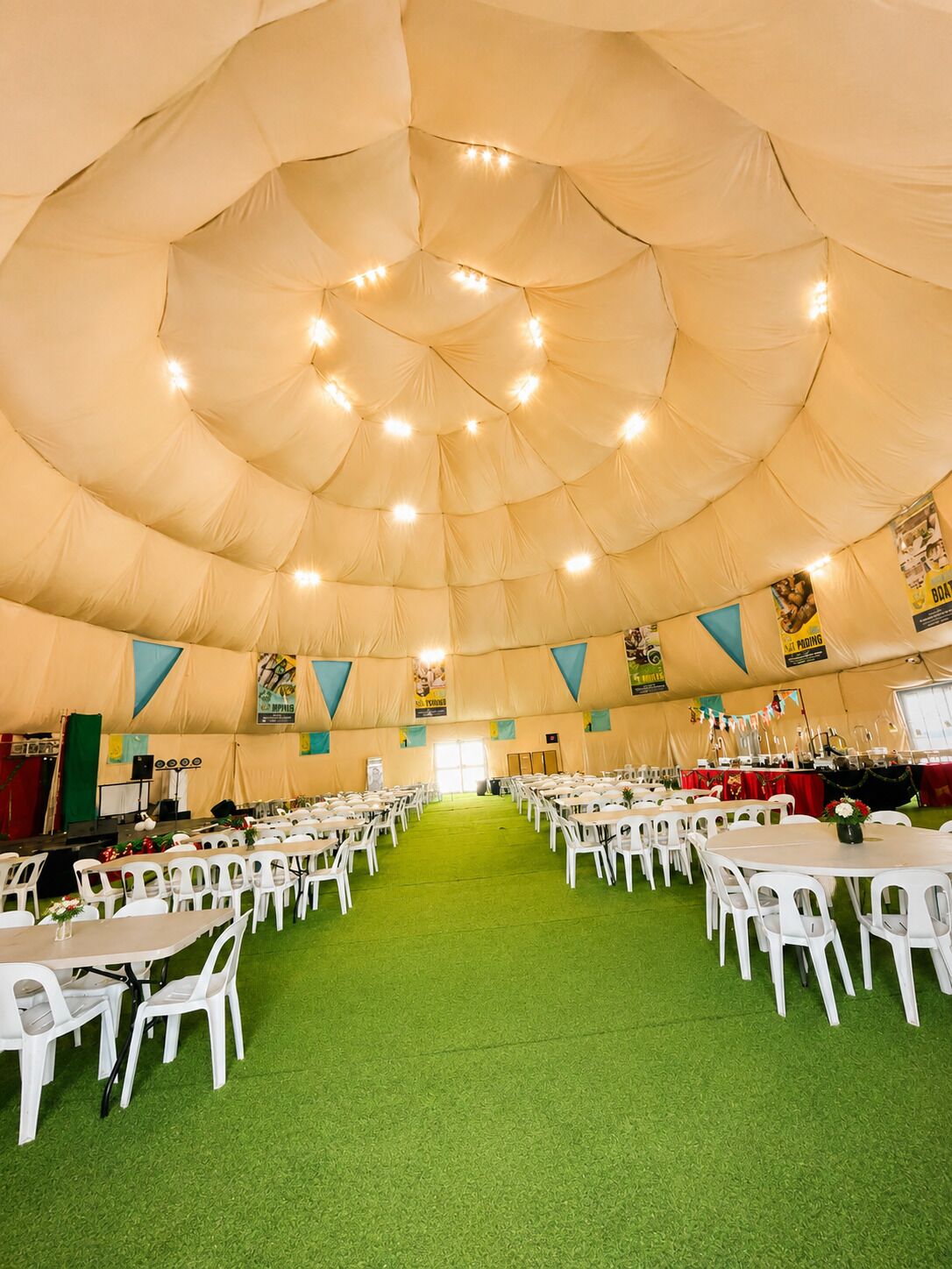 A large tent with a green floor, white chairs, and tables arranged in rows.