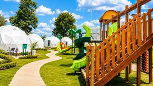 A playground with slides and a wooden climbing structure, surrounded by white dome-shaped buildings.
