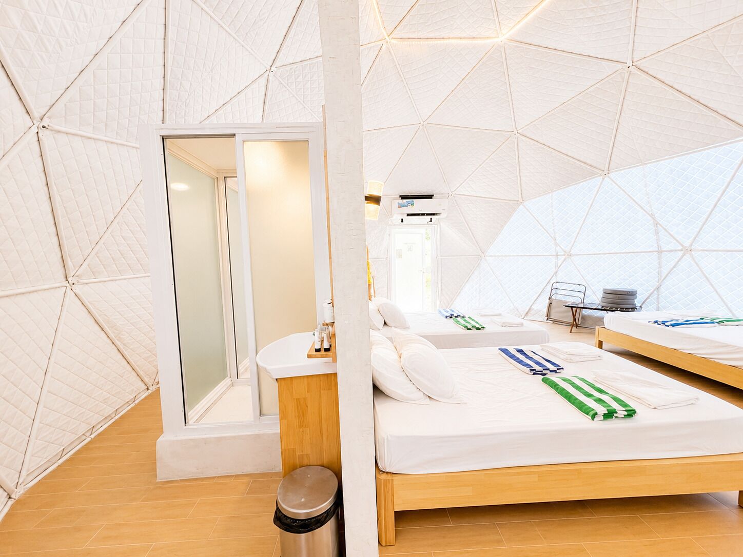 Un intérieur moderne aux lignes géométriques, avec un lit central, un petit coin salon et une salle de bain à l’aménagement apparent.