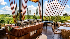 An outdoor dining area with a wooden bar, tables, and chairs, overlooking a lush landscape.