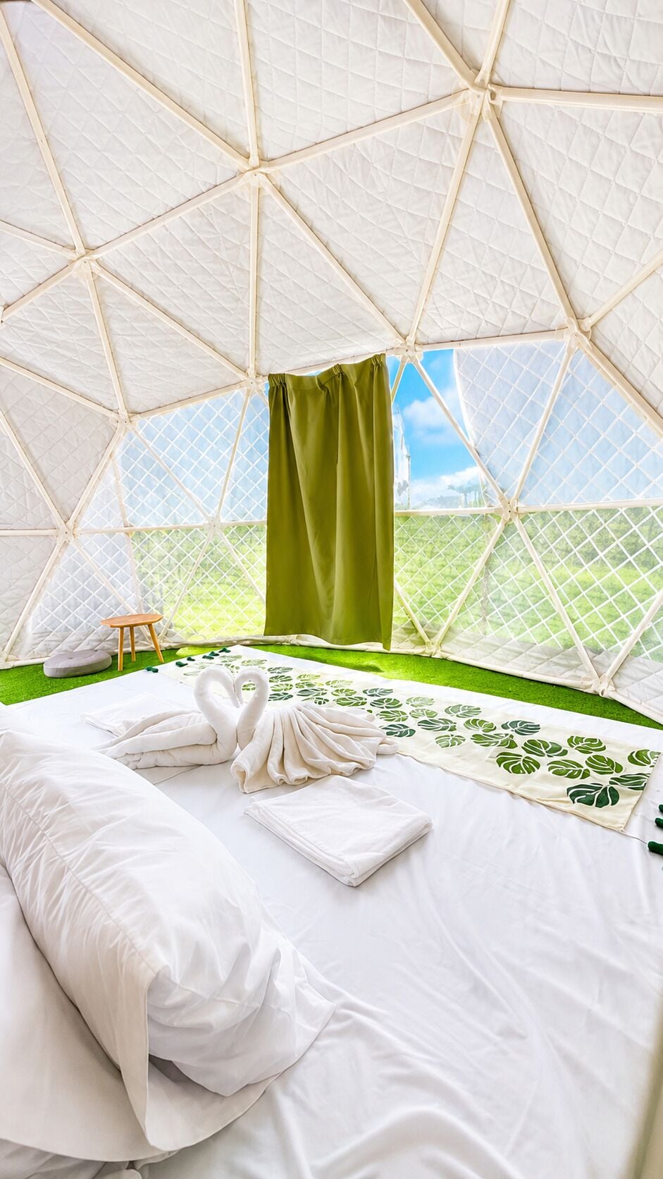 A tent-style room with a bed, green curtains, and a view of greenery outside.