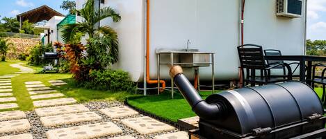 A barbecue grill, outdoor seating, and a house with a green roof.