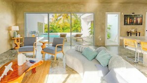 Una sala de estar moderna con sofá, sillones, una mesita de centro y vistas a una piscina y vegetación tropical.