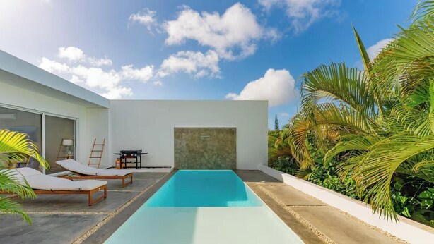 Un área de piscina moderna al aire libre con sillones de descanso, una parrilla y vistas al cielo.