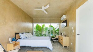 A bedroom with a bed, a ceiling fan, a dresser, and a window with a view of greenery. - Villa Bali - Sosua Mulata II (Sosúa)