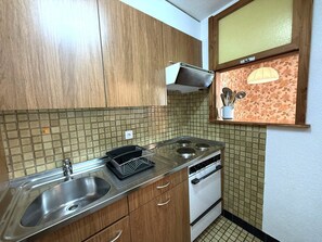 Een kleine keuken met een spoelbak, fornuis en een magnetron.