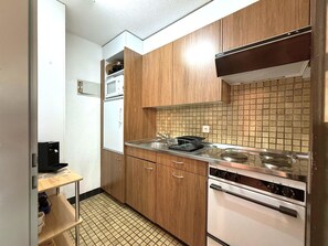 A compact kitchen with wooden cabinets, a microwave, a stove, and a tiled backsplash. - Royal 33 # 2-bed apartment, Dusche, WC 2-Bettwohnung, Dusche, WC by Interhome (Leukerbad)
