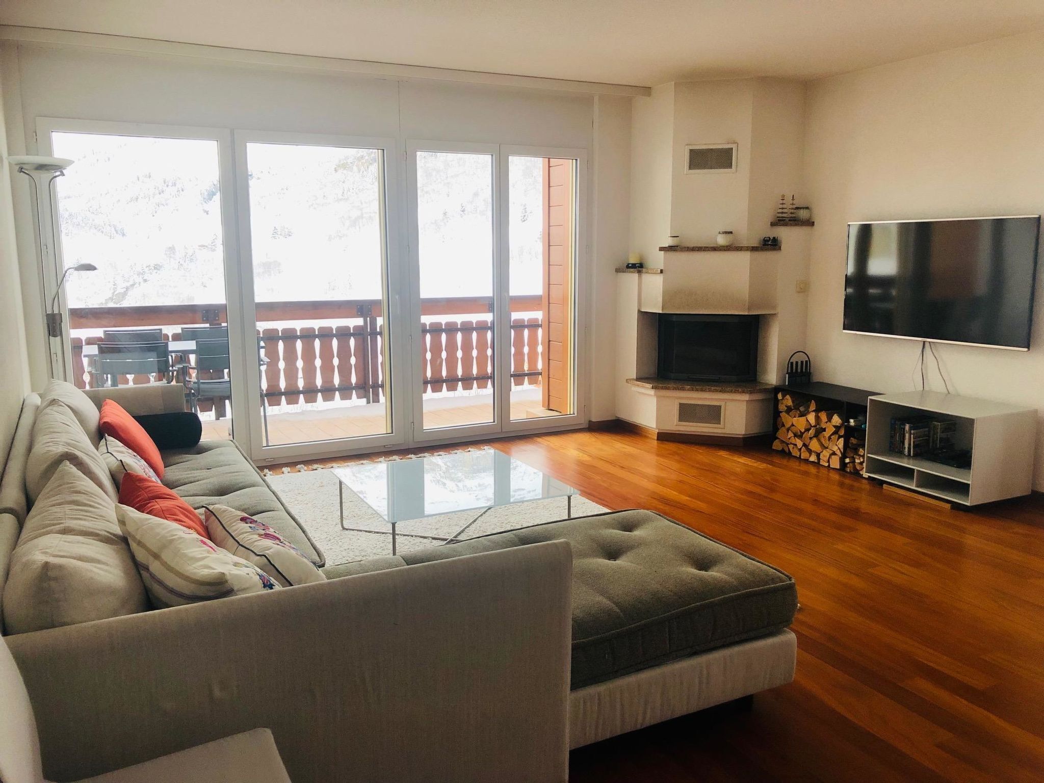 Ein Wohnzimmer mit einer Couch, einem Flachbildfernseher, einem Kamin und einem Balkon mit Gartenmöbeln.