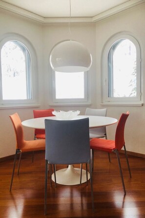 A dining area with a round table, six chairs, and three arched windows. - Edelweiss B 31 # 5-bed apartment, Dusche, WC 5-bed apartment, Dusche, WC by Interhome (Leukerbad)