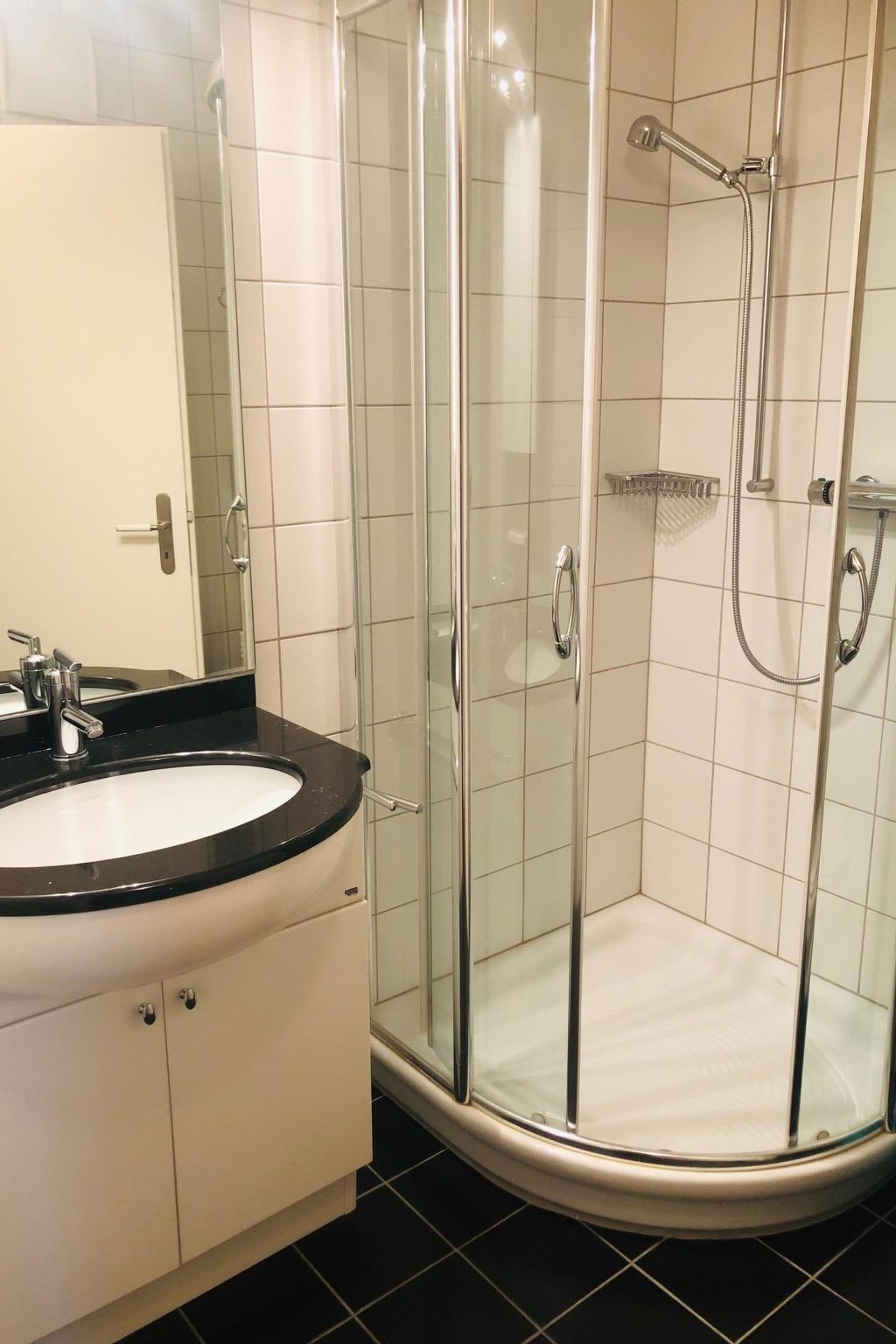 Ett badrum med en dusch som är avskärmad med glasväggar, en vit handfat med en svart bänkskiva och en spegel ovanför handfatet.