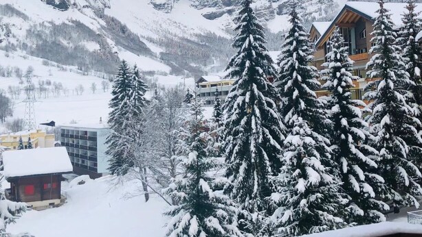 Un paysage montagneux enneigé avec une cabane en bois et un bâtiment doté d’un toit en pente.