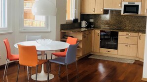 Une cuisine moderne avec des meubles en bois, un four encastré et un coin repas comprenant une table blanche et des chaises colorées.