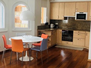 A modern kitchen with wooden cabinets, a built-in oven, and a dining area with a white table and colorful chairs. - Edelweiss B 31 # 5-bed apartment, Dusche, WC 5-bed apartment, Dusche, WC by Interhome (Leukerbad)