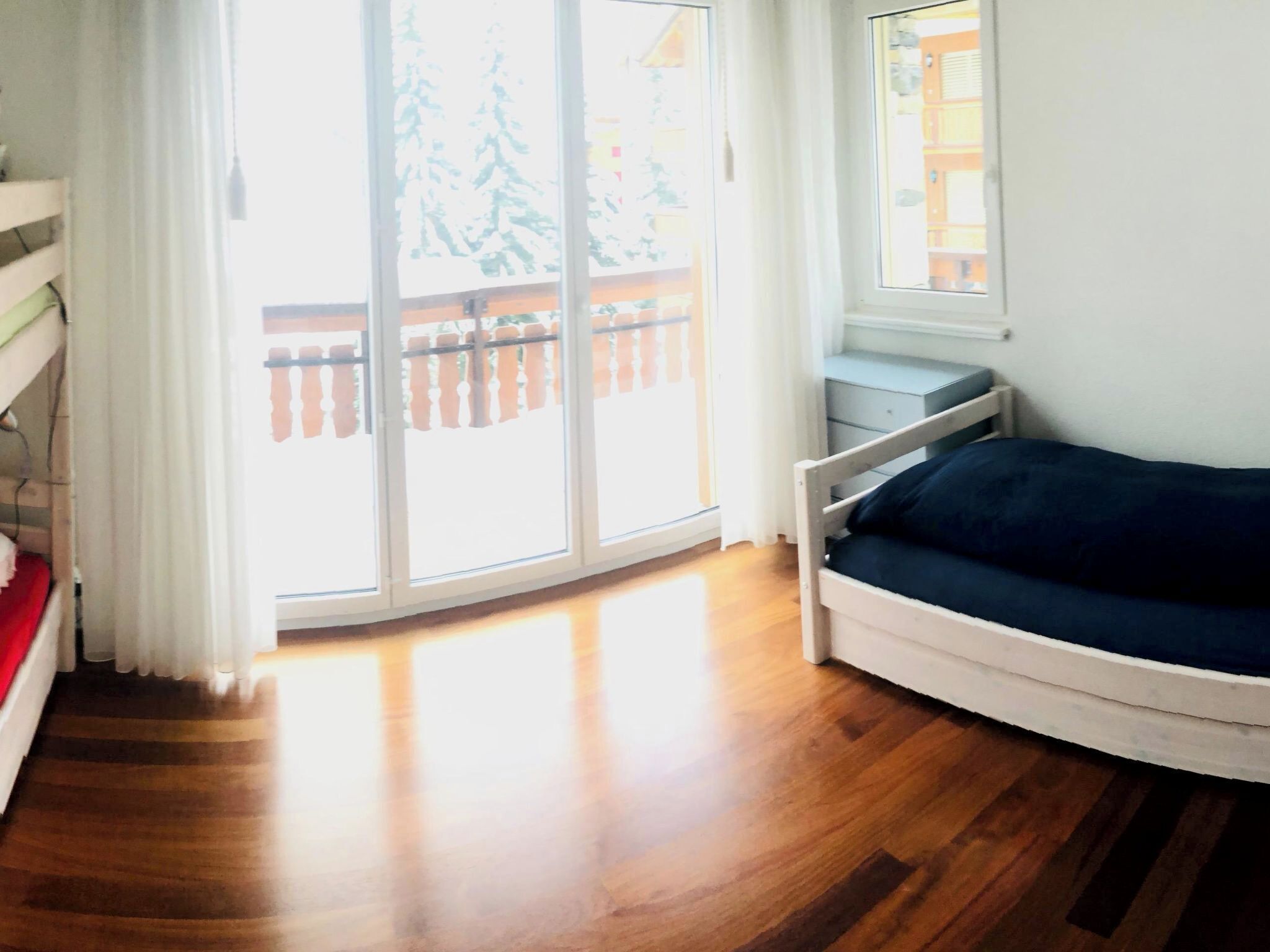 A room with a wooden floor, a blue sofa, a window with a view of trees, and a sliding glass door.