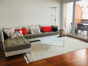 En moderne stue med sofa, sofabord og udsigt gennem en glasdør.
