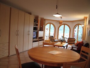 A dining area with a round wooden table, chairs, and a television in the background. - Château Leukerbad # 2-bed apartment, Dusche, WC by Interhome (Leukerbad)