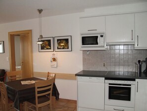 A compact kitchen with white cabinets, a microwave, a dishwasher, and a dining table with chairs. - Château Leukerbad # 2-bed apartment, Dusche, WC by Interhome (Leukerbad)