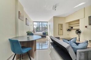 A modern living room with a sofa, a dining table, and a fan. - Urban Luxe Studio Illovo Mews by CTHA (Sandton)