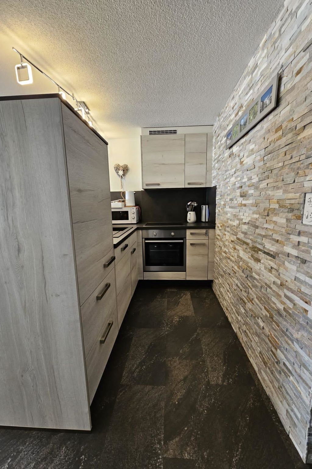 Cocina moderna con armarios de madera clara, horno empotrado y salpicadero de piedra.