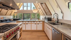 Una cocina moderna con una isla grande, electrodomésticos integrados y vistas a árboles a través de tragaluces.