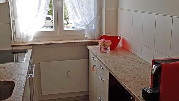 Una cocina con ventana, un calendario y un electrodoméstico rojo.