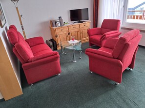 Ein Zimmer mit zwei roten Sesseln, einem kleinen Glastisch, einem Holzschrank mit Fernseher und einem Fenster mit Blick.