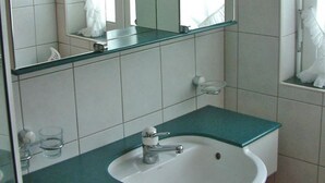 Un baño con un lavamanos blanco, un espejo y una repisa de vidrio.