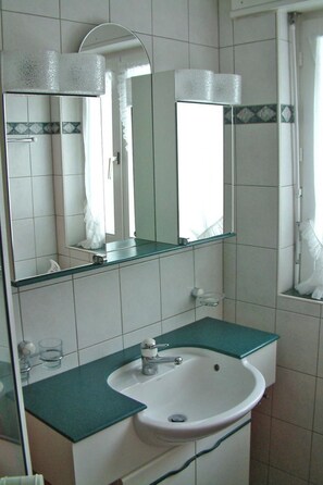 Ein Badezimmer mit einem weißen Waschbecken, einem Spiegel und einer Glasablage.