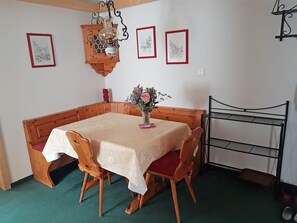 Ein Essbereich mit einem Holztisch und Bänken, einer Vase mit Blumen und gerahmten Bildern an der Wand.
