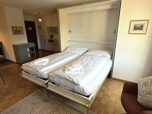 A double bed with a metal frame, a bedside table, and a small cabinet. - Royal 41 # 4-bed apartment, Dusche, WC 4-Bettwohnung, Dusche, WC by Interhome (Leukerbad)