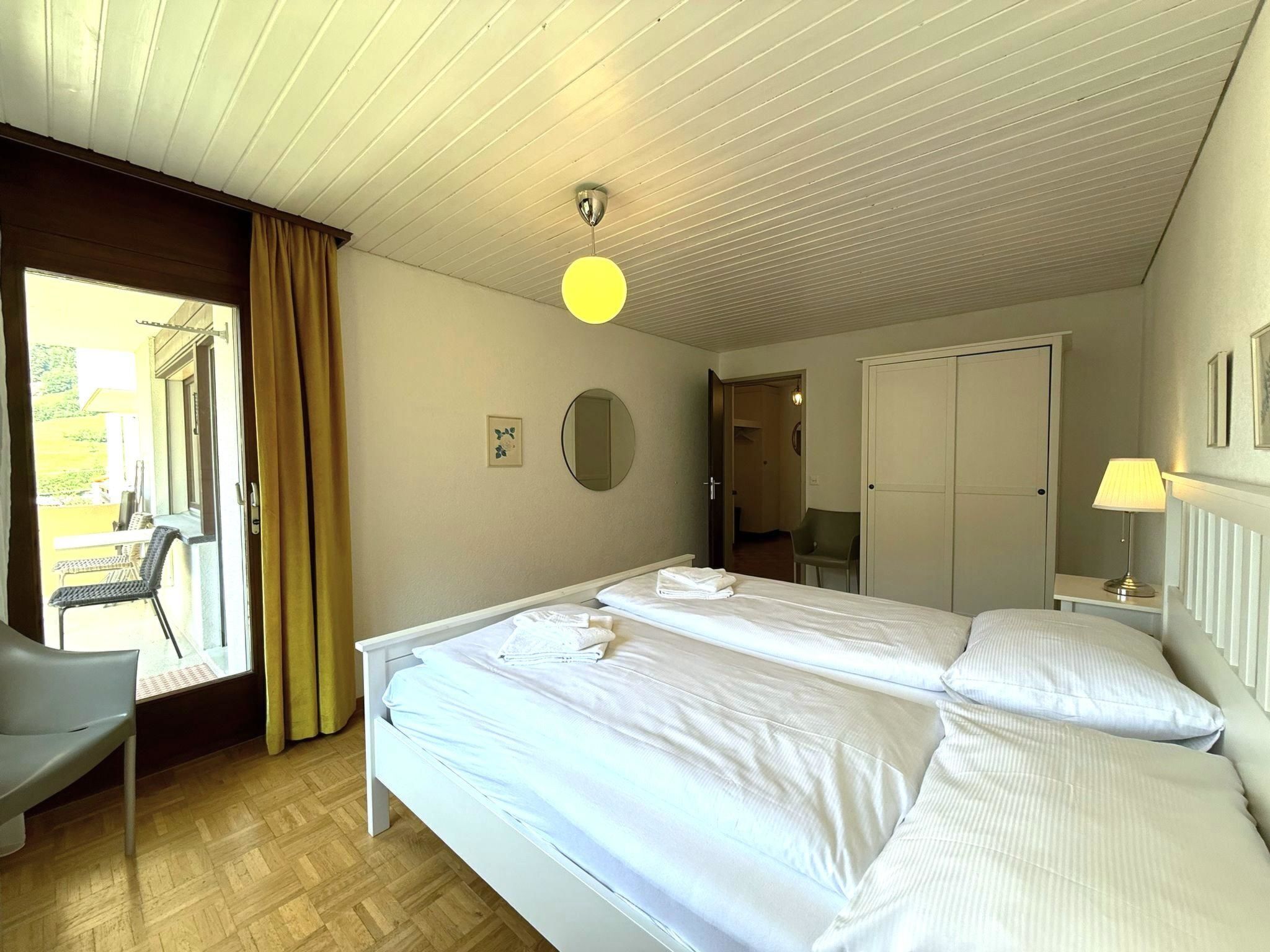 Een hotelkamer met twee bedden, een bureau, een stoel, een raam met gordijnen en een deur naar een balkon.