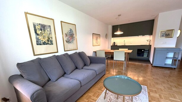 A modern living room with a grey sofa, a glass coffee table, and a kitchen in the background. - Royal 41 # 4-bed apartment, Dusche, WC 4-Bettwohnung, Dusche, WC by Interhome (Leukerbad)