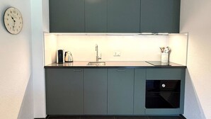 A compact kitchen with a single sink, a kettle, and a clock on the wall. - Royal 41 # 4-bed apartment, Dusche, WC 4-Bettwohnung, Dusche, WC by Interhome (Leukerbad)