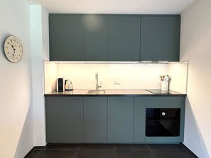A compact kitchen with a single sink, a kettle, and a clock on the wall. - Royal 41 # 4-bed apartment, Dusche, WC 4-Bettwohnung, Dusche, WC by Interhome (Leukerbad)