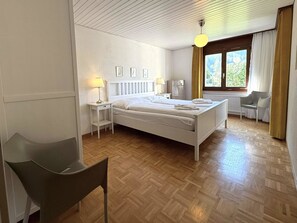A hotel room with a bed, bedside tables, a chair, a window with curtains, and a wooden floor. - Royal 41 # 4-bed apartment, Dusche, WC 4-Bettwohnung, Dusche, WC by Interhome (Leukerbad)