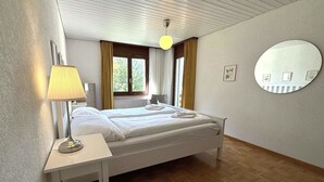 A hotel room with a bed, bedside table, lamp, and a round mirror on the wall. - Royal 41 # 4-bed apartment, Dusche, WC 4-Bettwohnung, Dusche, WC by Interhome (Leukerbad)