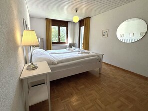 A hotel room with a bed, bedside table, lamp, and a round mirror on the wall. - Royal 41 # 4-bed apartment, Dusche, WC 4-Bettwohnung, Dusche, WC by Interhome (Leukerbad)