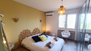 Een slaapkamer met een bed, nachtkastjes, een hanglamp, een radiator en een raam met uitzicht.