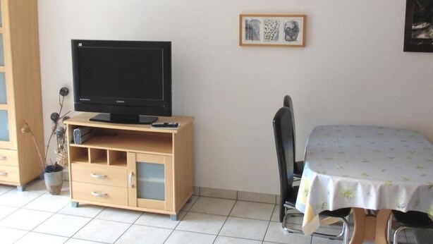 Una habitación con una televisión sobre un mueble de madera, una mesa de comedor con mantel, una silla y un aparador con cajones.