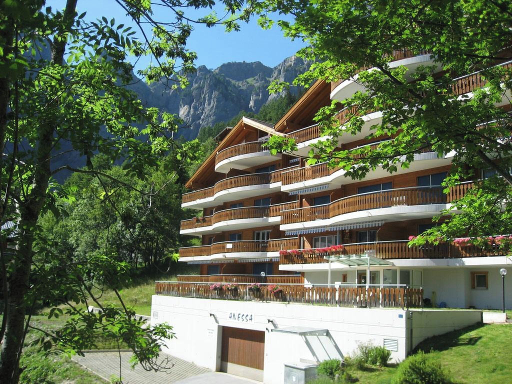 Ein mehrstöckiges Hotel mit Balkonen, umgeben von Grün und Bergen.