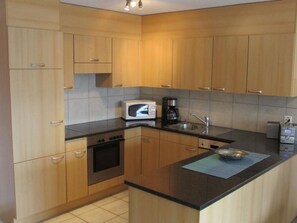 A kitchen with wooden cabinets, a microwave, a coffee maker, and a sink. - Anessa 33 # 4-bed apartment, Bad, WC 4-Bettwohnung, Bad, WC by Interhome (Leukerbad)